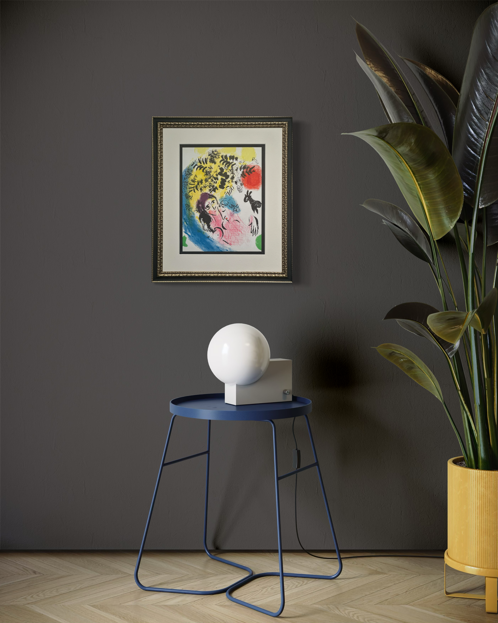 A framed abstract art print hangs on a dark gray wall in a styled room setting, featuring a blue side table with a white spherical lamp, a large potted plant, and light wood flooring.