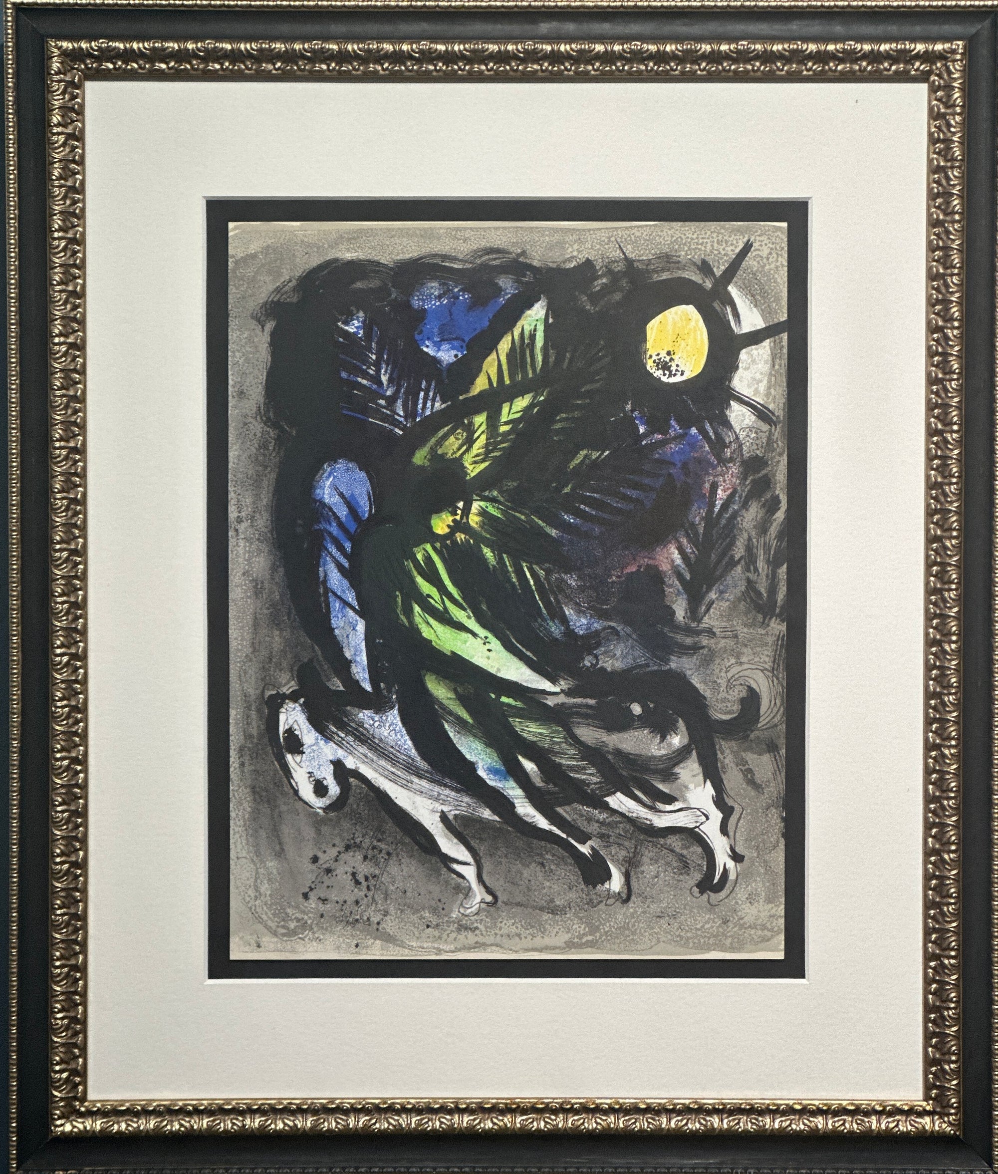 A framed abstract artwork featuring expressive black, blue, green, and yellow brushstrokes on a gray ground, surrounded by a wide white mat and an ornate black frame with gold detailing.