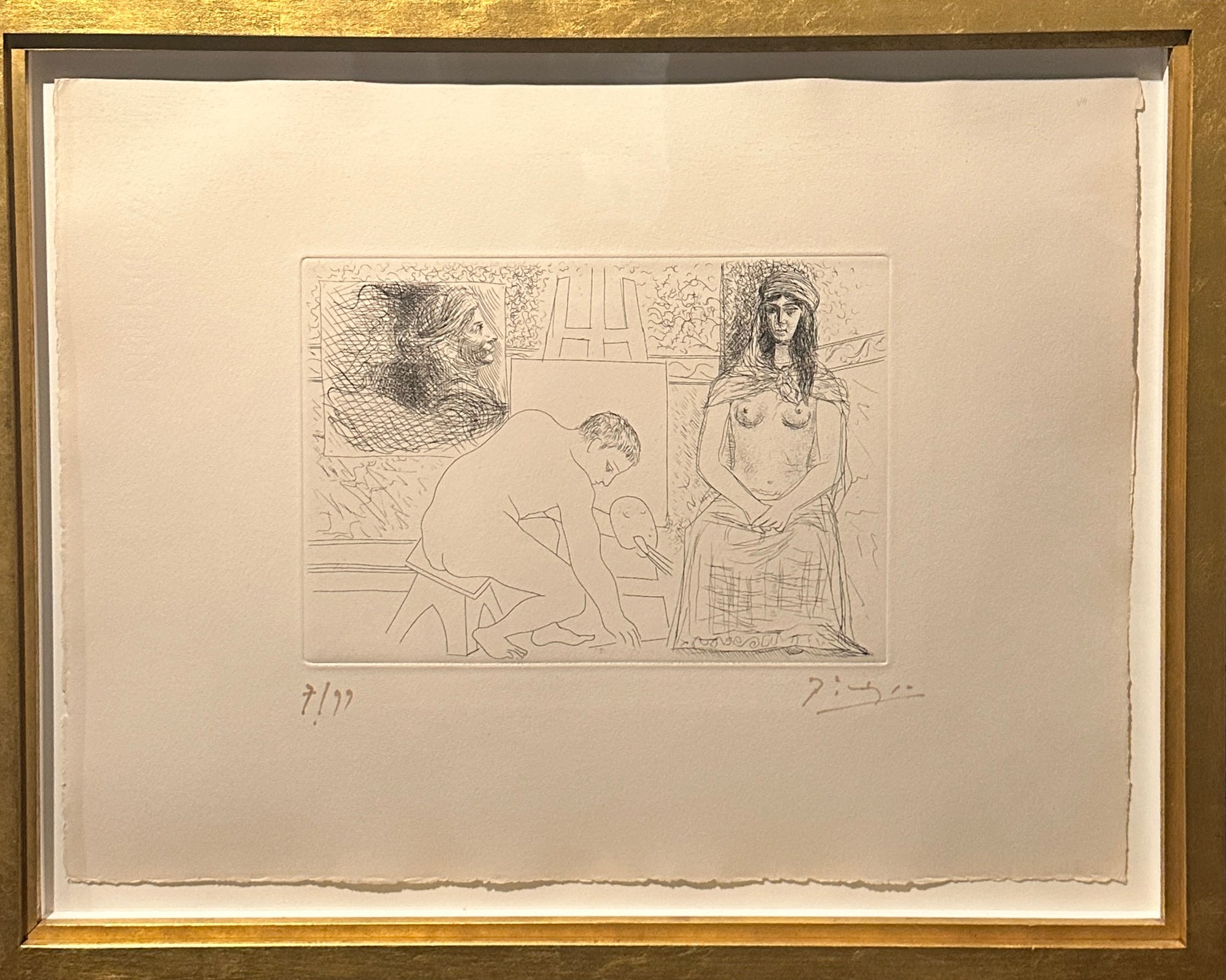 A framed monochrome art print or etching on a large off-white sheet, showing a sketch-like figure and seated figure in a room. The print is mounted with a wide white mat and surrounded by a gold-toned frame.