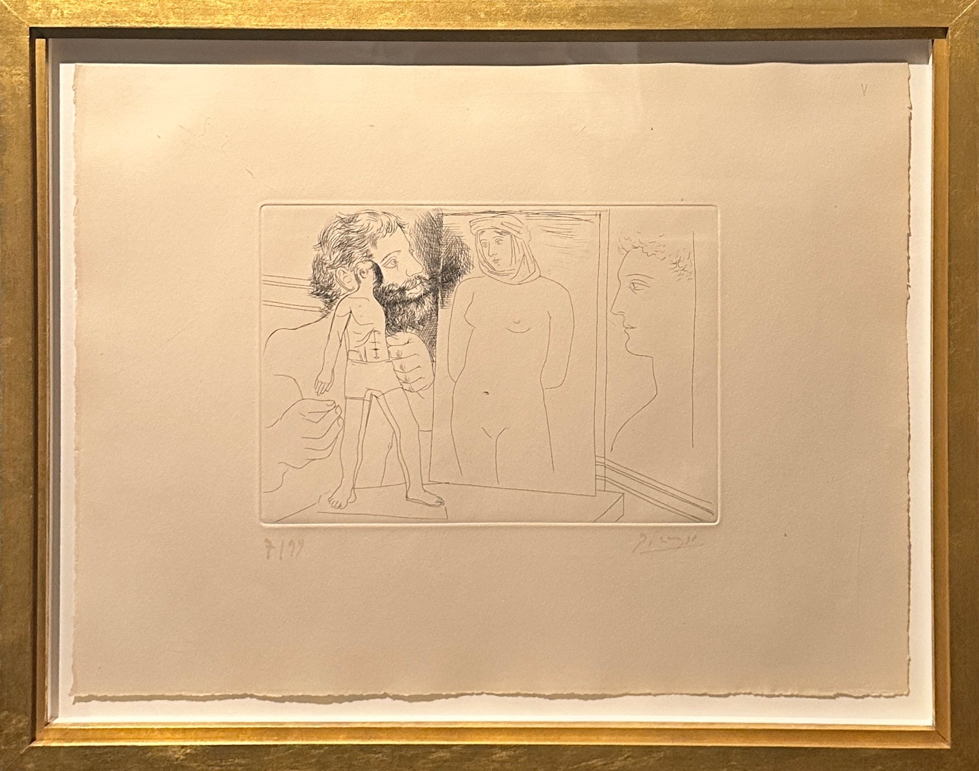 A framed monochrome art print or etching on warm off-white paper, showing three sketchy human figures and profile faces, surrounded by a wide white mat and a gold-toned frame.